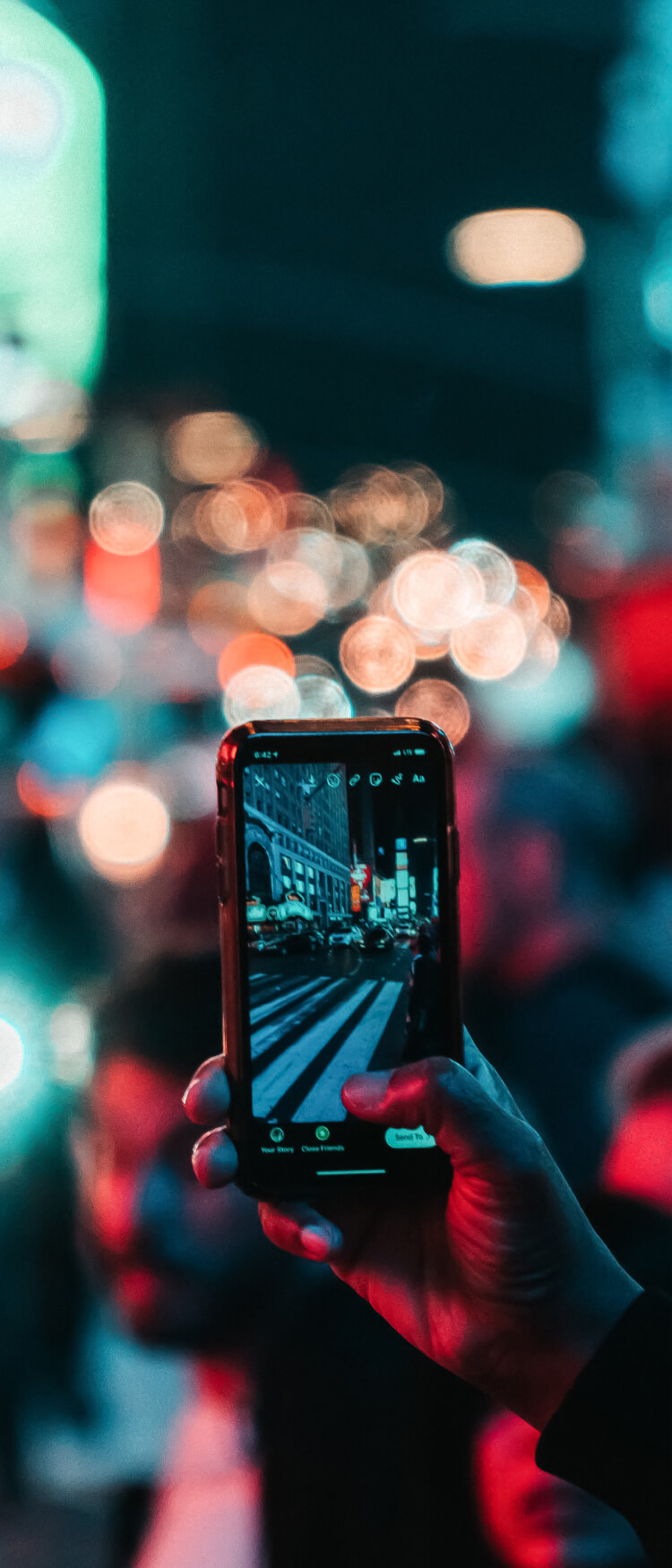 Zbliżenie na dłoń z telefonem. Zdjęcie miasta nocą, w tle rozmazane refleksy światła ulicznych latarni.